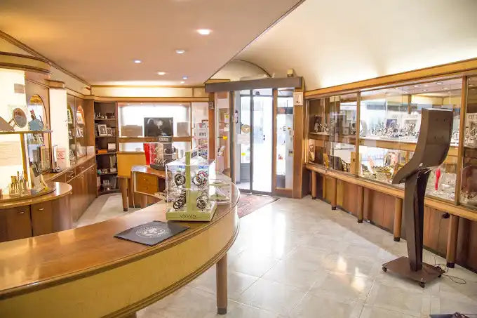 Un negozio ben illuminato, organizzato di gioielli e orologi con vetrine in legno e un banco servizio.